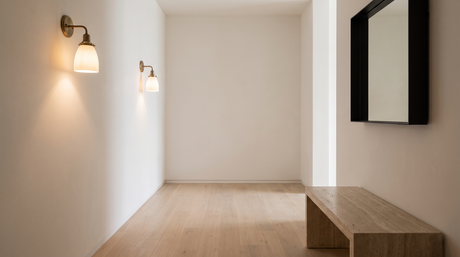Pair of milk glass wall sconces lighting a plaster hallway wall above an oak bench