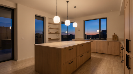 Three milk glass pendant lights hanging in a row above a pale oak kitchen island at dusk